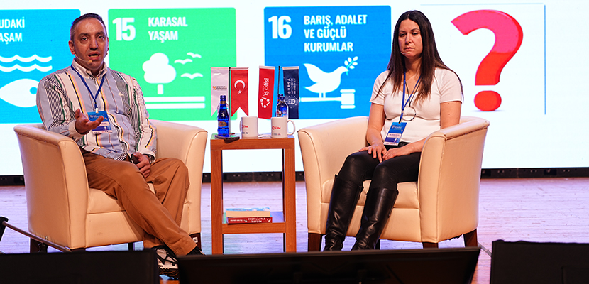 Sahnede iki kişi yan yana oturuyor; solda Mehmet Kızıltaş, sağda Güler Koca. İkisi de bej koltuklarda, aralarında su şişeleri, küçük bir Türk bayrağı ve birkaç kitabın bulunduğu ahşap bir sehpa yer alıyor. Arkadaki büyük ekranda ise Sürdürülebilir Kalkınma Amaçlarına ait renkli simgeler görünüyor. Sahne genel olarak sakin, profesyonel ve bilgi paylaşımına odaklı bir panel atmosferi taşıyor.