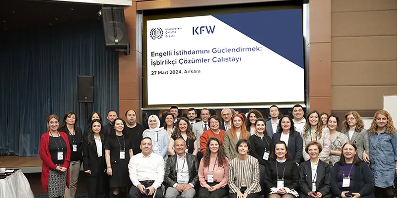 Betimleme: Sahnede ayakta ve sandalyede çalıştaya katılan tüm grupların yan yana toplu çekilen resmi.